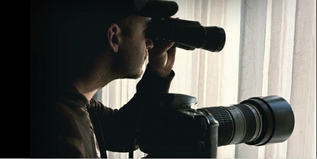 Un agent observant aux jumelles à côté d'un appareil photo à long téléobjectif